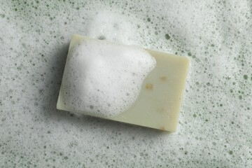 Soap and fluffy foam on green background, top view