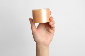 Woman holding jar of face cream on white background, closeup
