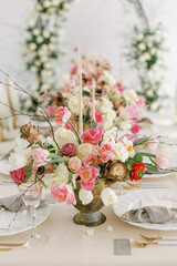 Table decorated for a wedding celebration. Bouquets of pink, white and peach flowers, vintage decor. White bright room, an arch of rose flowers