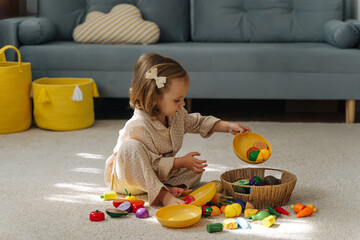 A little girl playing with wooden fruits and vegetables  on floor  in nursery. Educational games,...
