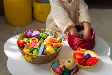 A little girl playing with  wooden fruits and vegetables on the table in nursery. Educational...