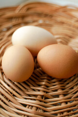 Three chicken eggs of different colors and different sizes lie in a wicker basket