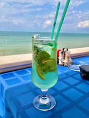Mojito in a beautiful glass on the background of the sea. Green drink cocktail on a blue tablecloth