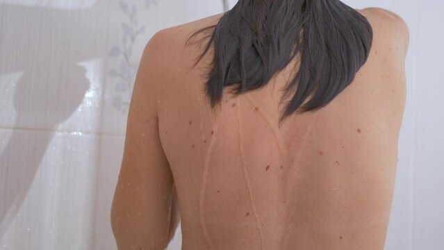 Naked woman with long hair takes a shower. Reasonable waste of water on water procedures. Morning routine in white bathroom.