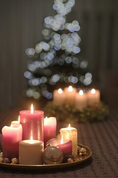 Sieben angemachte, hell rote Kerzen stehen  auf einem goldenen Tablett, vor einem Tannenbaum mit angemachte Beleuchtung, unscharf in Hintergrund.