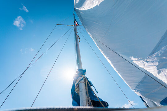 imagen con vista inferior de el m&aacute;stil de un velero en un d&iacute;a soleado y su vela mayor ondeando por el viento