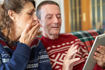 Mother sending kisses with father holding tablet during family Christmas video call