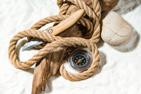 Survival In Extreme Conditions Concept With Rope, Compass And Knife Lying On A Weathered Wooden Log.