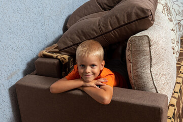 Boy looks out of house from pillows on sofa. Sense of security, game of hide and seek. Selective focus.