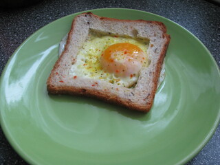 Fried egg on a green plate. A fried egg in the middle of a piece of bread.