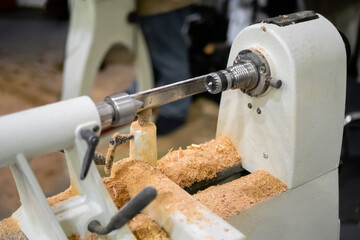 Close up view: wood turning lathe machine with shavings at workshop. Carpentry, industrial, woodwork and manufacturing concept