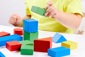 A child plays with playful colored geometric shapes on a light table. The child builds towers from toy building bricks. selective focus