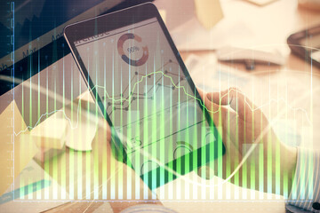 Double exposure of man's hands holding and using a phone and financial graph drawing. Analysis concept.