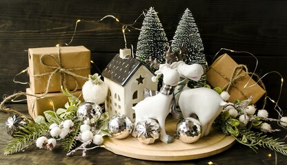 Decorative home decoration for Christmas and New Year.  Small green fir trees, figurines of white deer, fir branches, eco-style holiday gifts.  Foreground, wooden background, background pattern.