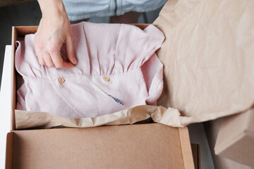 woman packs children's clothes, a pink dress in boxes. small business and entrepreneurship. a business woman sends an order for delivery. an online clothing store. kraft cardboard box