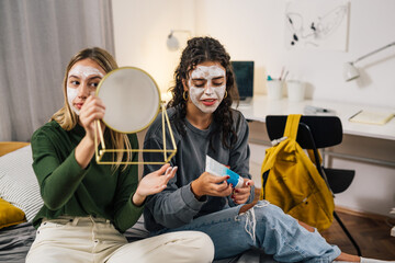 teenager friends applying cosmetic cream on face in dorm room