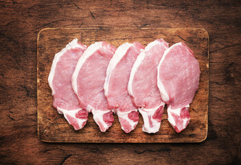 Raw pork chops, meat on rustic wooden cutting board prepared for cooking with garlic, thyme, spices...