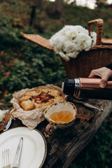 picnic in the forest on a cold cloudy day. pouring hot tea from a thermos into an outdoors ceramic cup.
