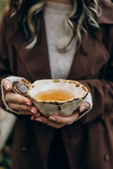craft ceramic cup with herbal tea in female hands close-up. warm your hands with hot tea on a cold cloudy day.	