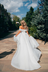 Fototapeta na wymiar a blonde bride running down a path in the park in a white long dress.