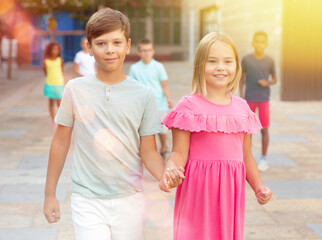 European boy and girl walking together hand in hand through city streets in summertime.