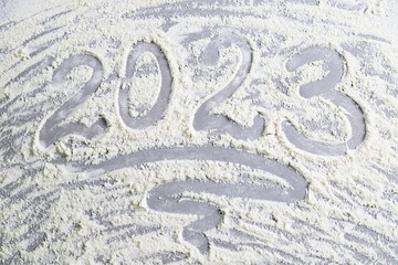 The numbers 2023 are handwritten on scattered flour on a gray stone surface. High-quality photo. Top view. Concept: New Year and Christmas 2023.
