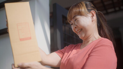 Fototapeta na wymiar Asian woman rejoices in receiving a parcel in front of her house.