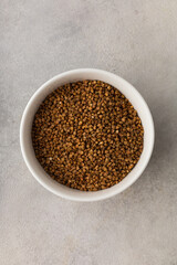 A bowl of dry buckwheat before cooking on a light gray background