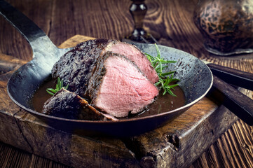 Traditional German venison roast with juniper berry and rosemary in spicy red wine sauce served as...