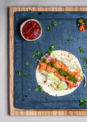 Healthy breakfast concept. Salmon, lettuce, herbs and pesto sauce on a tortilla. Wooden board. Tasty food in restaurant. Top view.