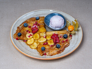 Close-up of a sweet dessert in a restaurant. Pancakes with maple sauce, banana slices and berries. Ice cream ball.
