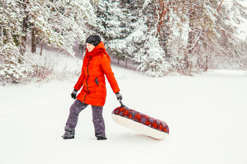 a girl in a red jacket holds a tubing and laughs in winter against the backdrop of a snowy forest