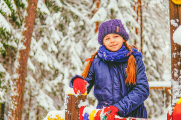 a girl in a blue jacket is standing in the forest laughing in winter against the backdrop of a snowy forest