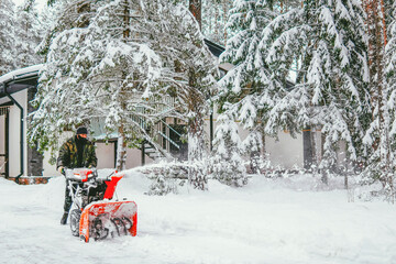 a man cleans the road from snow with a snowplow in the forest in winter against the backdrop of a...