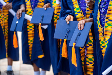 selective focus of african people, in uniform holding hat, colourful black people in traditional wear standing in line outside- graduation concept - obrazy, fototapety, plakaty