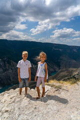 Teen boy with his sister stands on the cliff of scenic Sulak canyon in Dagestan