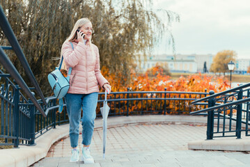 A blonde girl speaks on the phone and walks around the city against the backdrop of autumn leaves and laughs on a sunny day