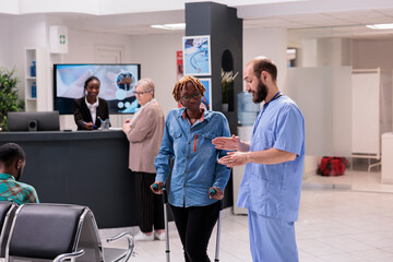 Hospital administrative staff guiding african american patient with degenerative disease to therapist office. Afro female receptionist at sanatorium supporting elderly woman. - obrazy, fototapety, plakaty