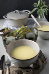 Closeup view of a creamy asparagus soup in a ceramic bowl over a dinner table.