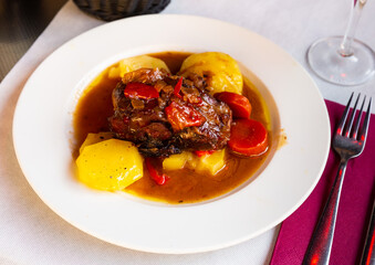 Baked lamb shoulder with vegetables and sauce served on white plate