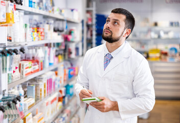 Portrait of male druggist making notes while working in drugstore.