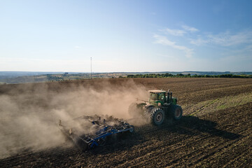 Aerial view of tractor plowing agriculural farm field preparing soil for seeding in summer