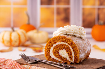 Pumpkin roll on a rustic wooden cutting board in an autumn kitchen scene with pumpkins out of focus...