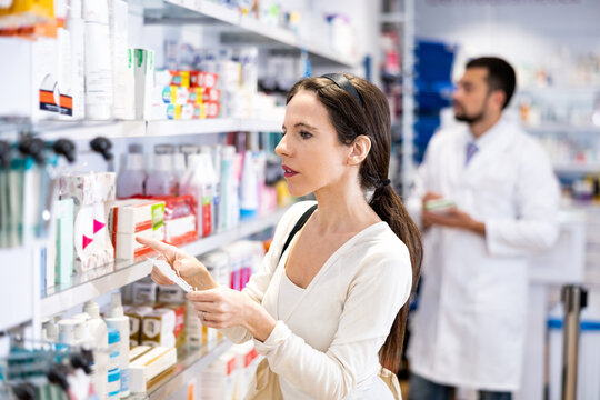 Focused young woman choosing products with shopping list at drug store