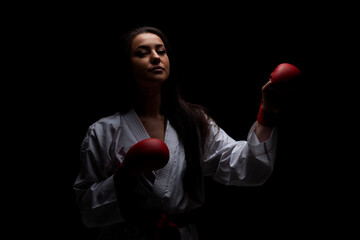 girl exercising karate punch wearing kimono and red gloves against black background
