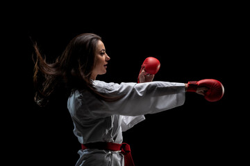 girl exercising karate punch wearing kimono and red gloves against black background