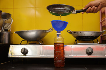 Close up of a man's hands recycling edible oil from a frying pan into a plastic bottle in his home...