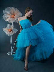 Portrait of a beautiful young woman with long hair in a lush blue tulle dress in the studio against...