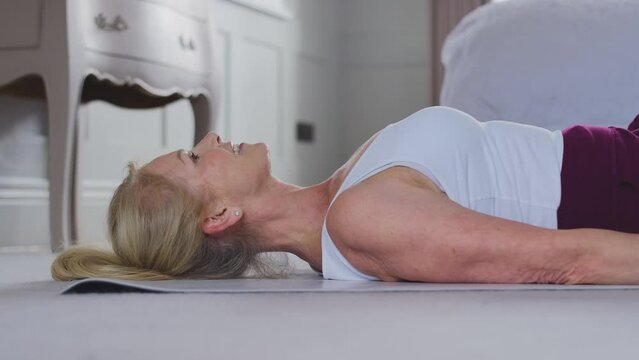 Active mature woman exercising doing yoga on mat at home - shot in slow motion