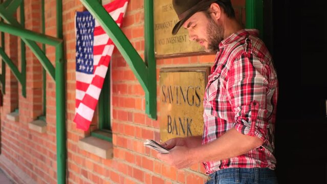 Texas banker in the wild west gives a loan from the money vault. a cowboy in a plaid shirt in the Populated western town sits at a tavern and counts money. Street of wild west town with bank building
